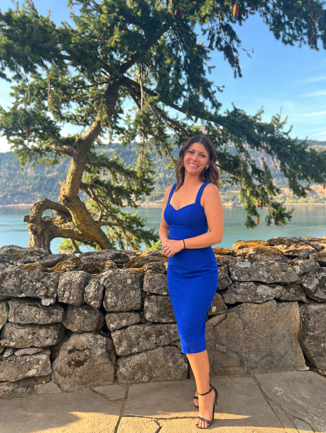 Christine in a blue dress beside a stone wall overlooking the Columbia River